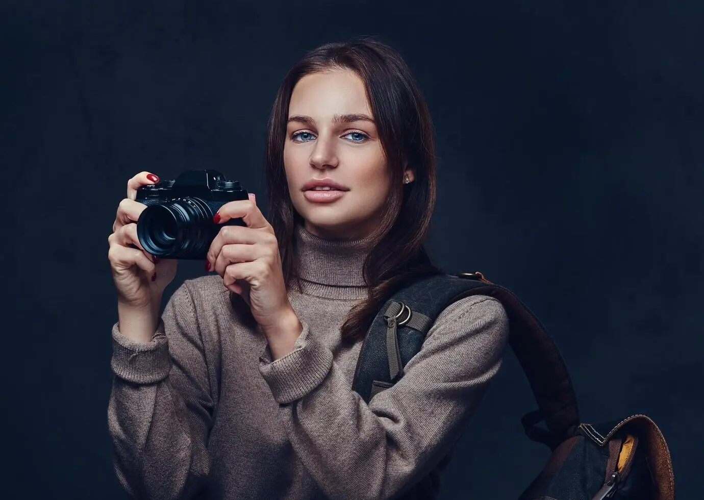 A brunette female traveler carrying a backpack is holding a compact photo camera.